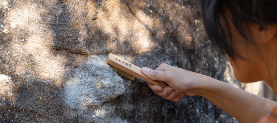 person brushing chalk off outdoor boulder